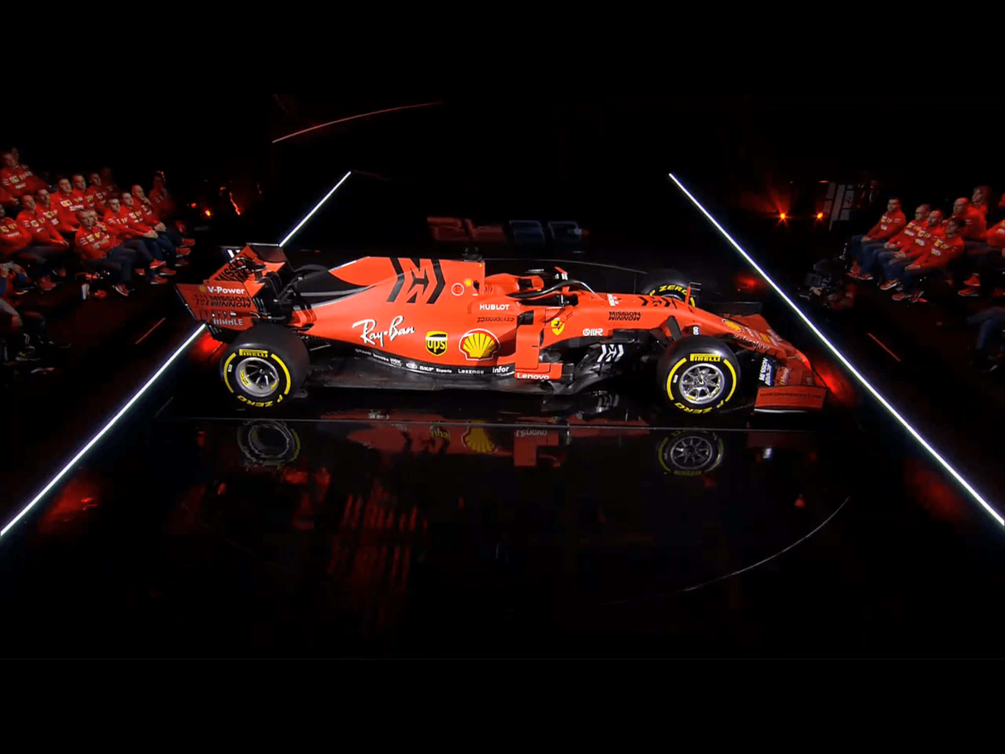 Racing 桌布 壁紙 — 一架充滿活力的橙色一級方程式賽車在反射舞台上，在明亮的白色燈光下，與身穿紅色的坐席觀眾一同戲劇性地展示。