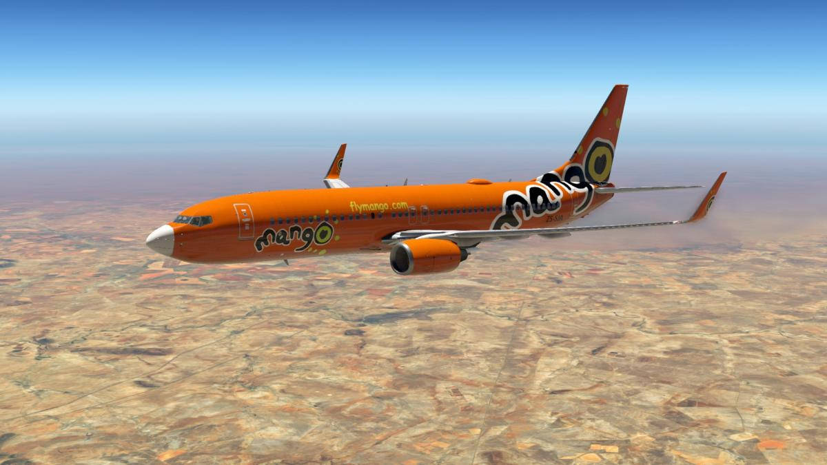 飛機 桌布 壁紙 — 一架充滿活力的橙色芒果航空(Mango Airlines)飛機在晴朗的藍天下翱翔於廣闊的沙漠景觀之上。