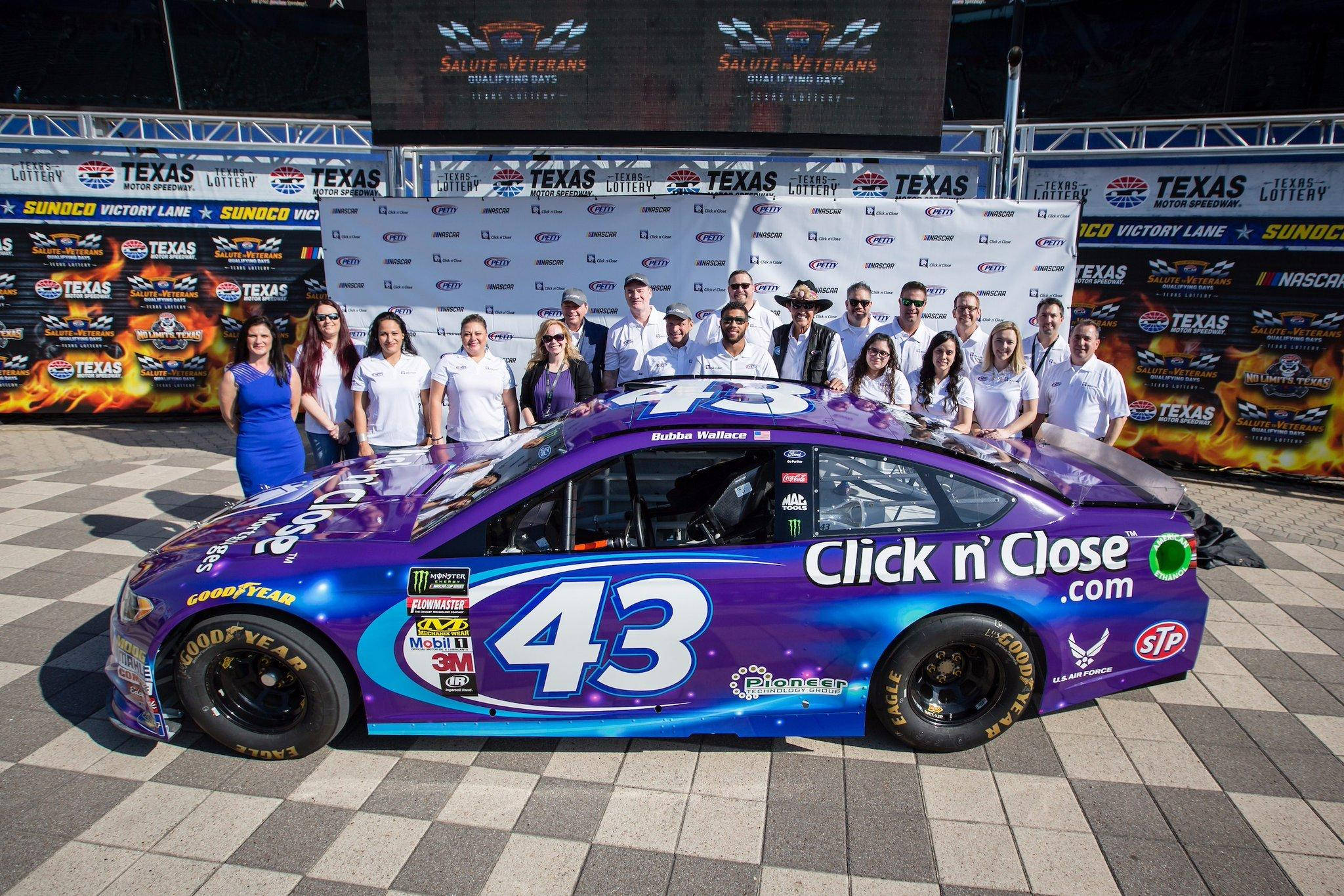 Bubba Wallace 桌布 壁紙 — 一架充滿活力的紫色和藍色NASCAR賽車，編號43，停放在棋盤格路面上，車隊在德州賽車場後方擺姿勢。