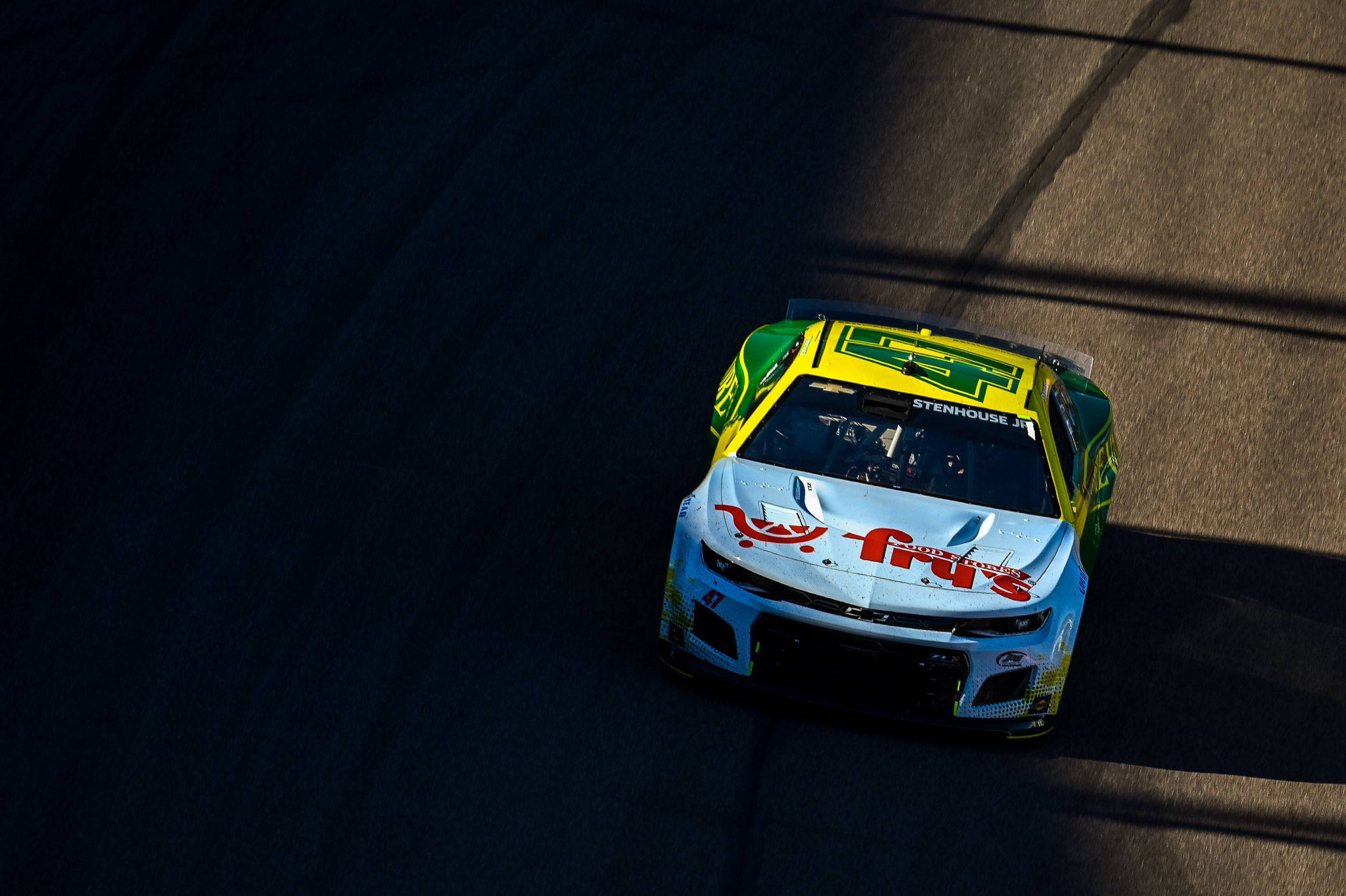 Racing 桌布 壁紙 — 一架充滿活力的綠色、黃色和白色賽車在陽光照耀的瀝青賽道上飛馳，投下長長陰影的鳥瞰圖。