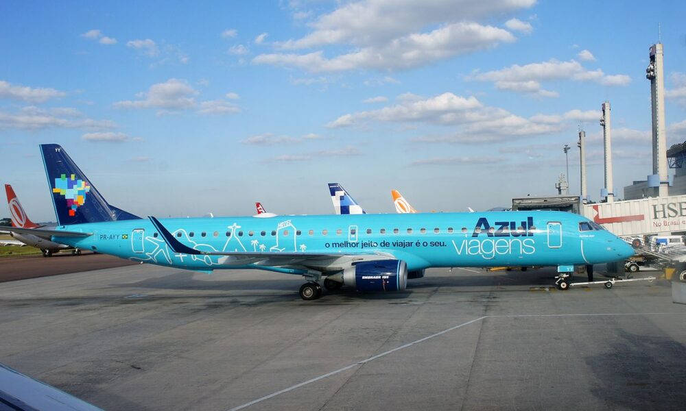 巴西 桌布 壁紙 — 一架充滿活力的藍綠色Azul Airlines飛機帶有旅行主題藝術品，停在機場停機坪上，天空部分多雲。