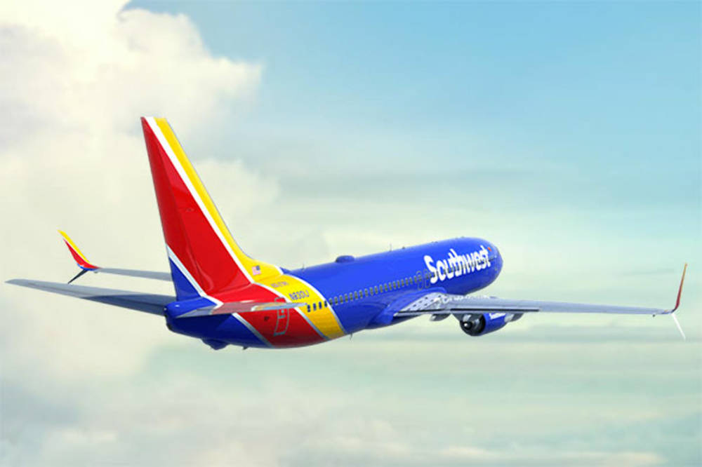 flying 桌布 壁紙 — 一架充滿活力的西南航空噴射機，以醒目的藍、紅、黃塗裝，在部分多雲的天空中翱翔。