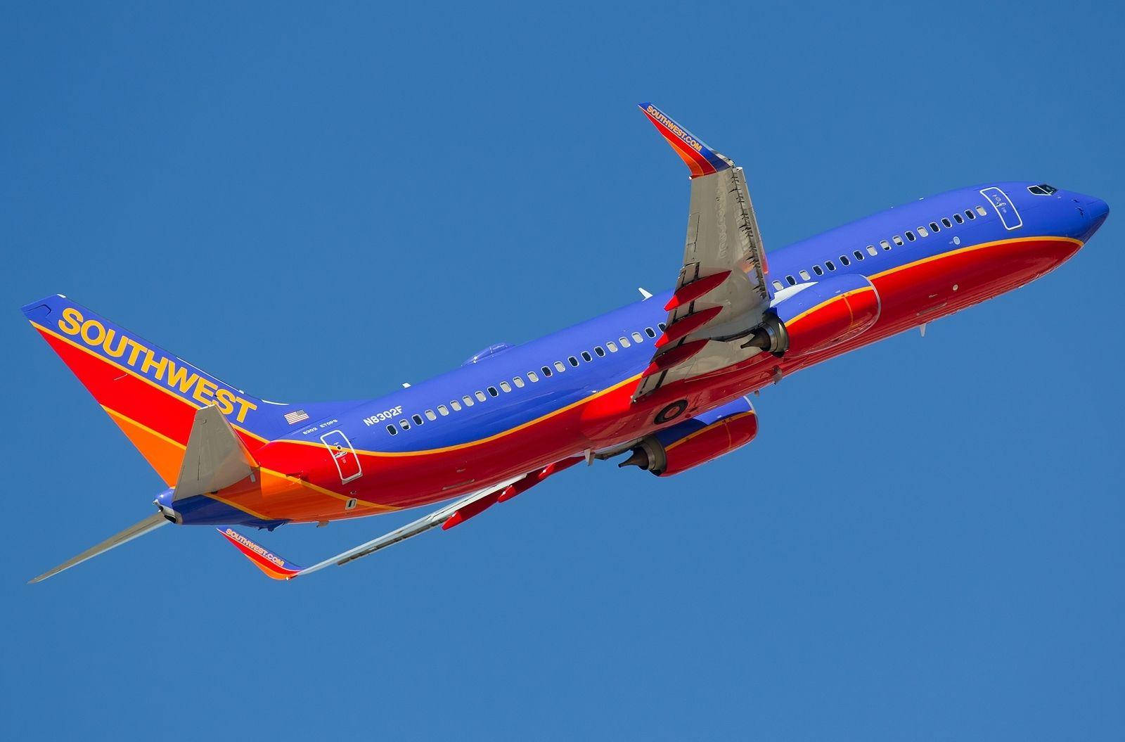 Plane 桌布 壁紙 — 一架充滿活力的西南航空噴射機在清澈的藍天中翱翔，帶有醒目的紅、藍和橙色塗裝。