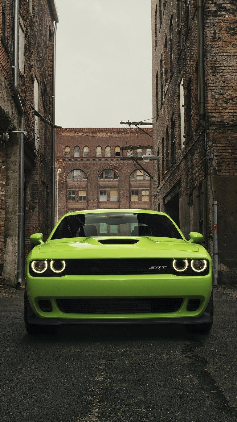 Challenger 桌布 壁紙 — 一架充滿活力的青檸綠色 Dodge Challenger SRT 停泊在兩棟風化建築物之間的狹窄磚砌小巷中。