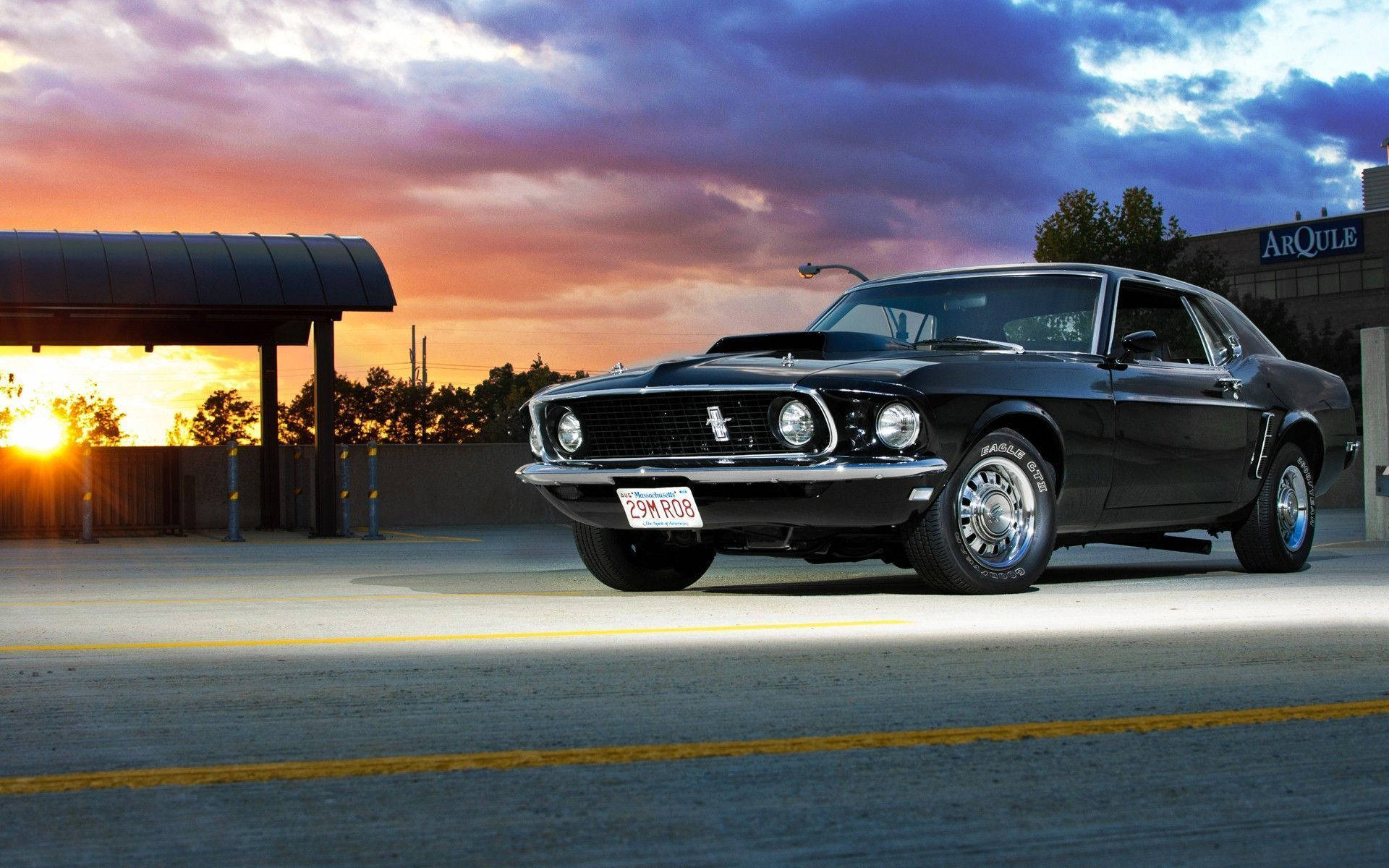 Ford Mustang 桌布 壁紙 — 一架光滑的黑色經典野馬在戲劇性的日落天空下閃耀，天空有火橙色雲彩和深紫色色調。