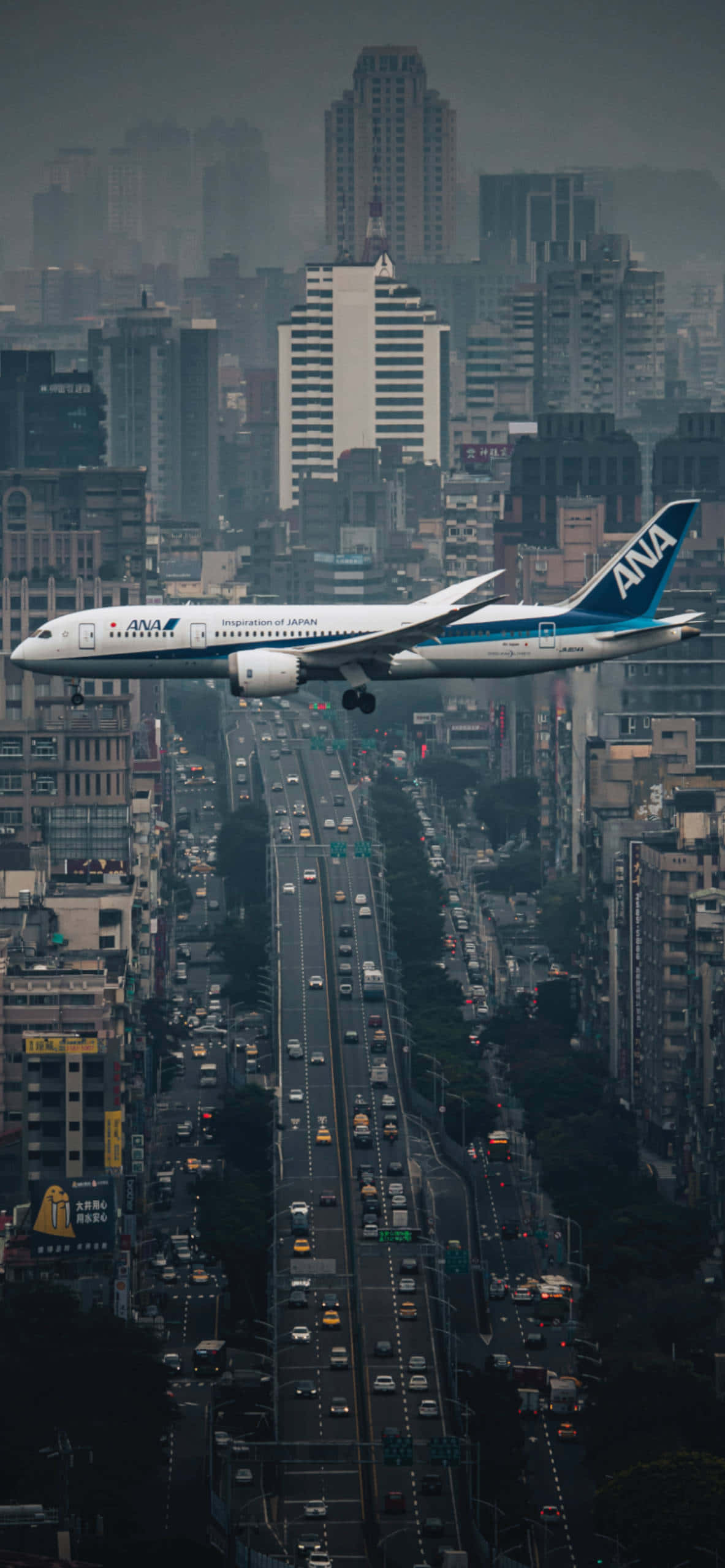 桌布 壁紙 — 一架全日空飛機在煙霧瀰漫的天空下，低飛過一條車水馬龍、高樓林立的繁忙城市街道。