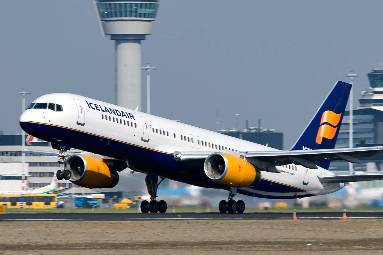  壁紙 — 一架冰島航空波音757，配備橙色引擎，在朦朧天空下滑行於跑道，背景是機場控制塔。