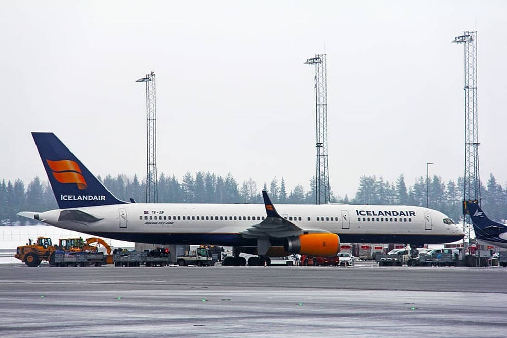 Airport 桌布 壁紙 — 一架冰島航空波音757停放在濕滑的停機坪上，周圍有地勤車輛和高聳的機場塔台，天空多雲。