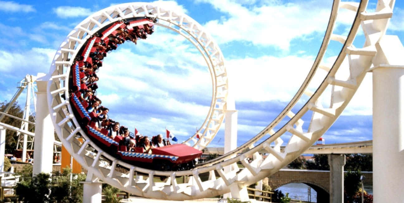 Roller Coaster 桌布 壁紙 — 一架刺激的紅色雲霄飛車載著乘客尖叫著穿過一個巨大的白色環圈，背景是晴朗的藍天和蓬鬆的白雲。