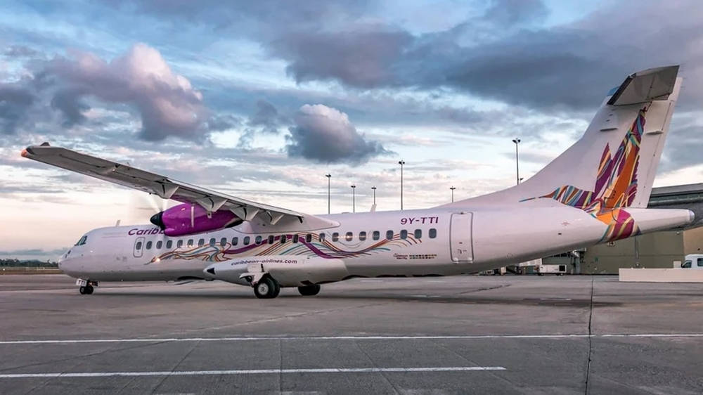  壁紙 — 一架加勒比航空ATR 72渦輪螺旋槳飛機，帶有紫色和橙色塗裝，停在機場停機坪上，天空多雲，暮色蒼茫。