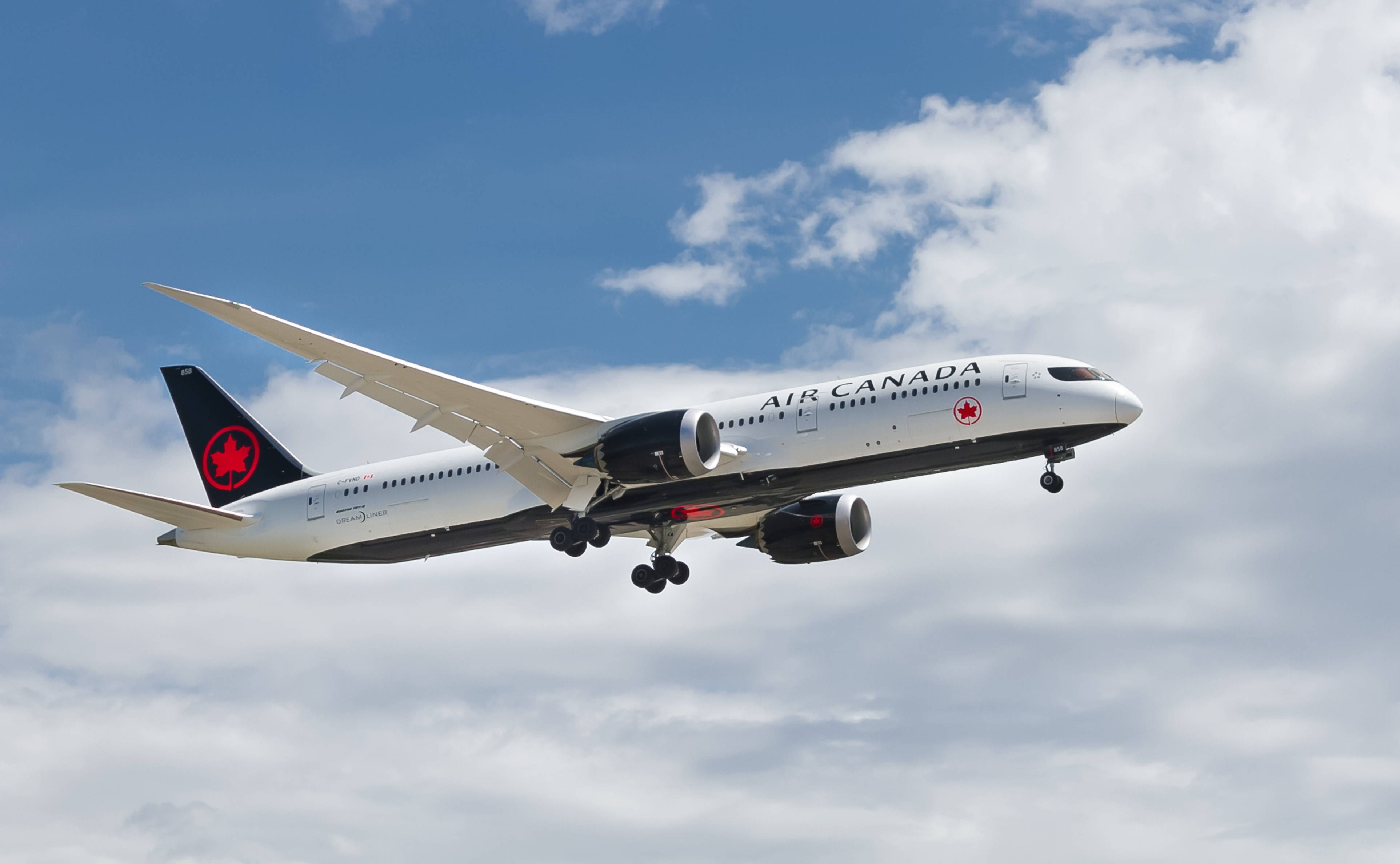 飛機 桌布 壁紙 — 一架加拿大航空的飛機放下起落架，在點綴著蓬鬆白雲的明亮藍天中翱翔。