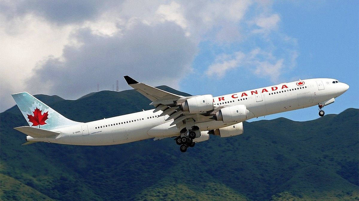 山脈 桌布 壁紙 — 一架加拿大航空飛機正在下降，起落架放下，背景是綠色的山脈和部分多雲的藍天。