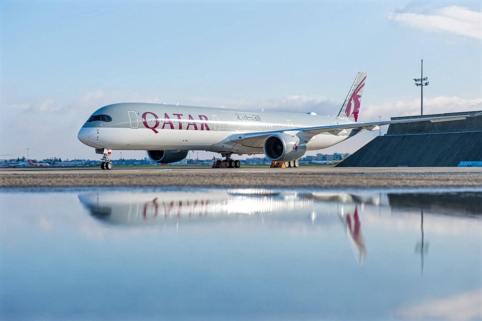 飛機 桌布 壁紙 — 一架卡塔爾航空空中巴士A350停在機場停機坪上，其倒影映照在清澈藍天下的一個水坑中。