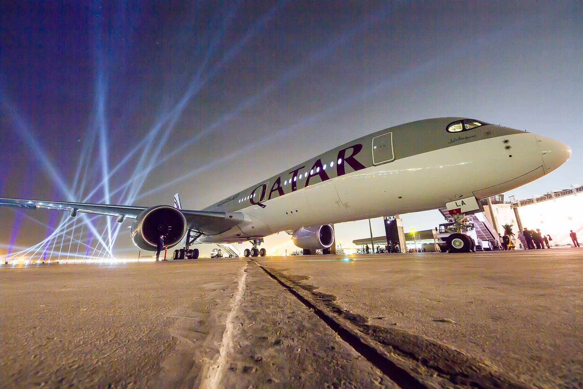 飛機 桌布 壁紙 — 一架卡塔爾航空飛機在夜間停機坪上被戲劇性的藍色聚光燈照亮，附近有人。