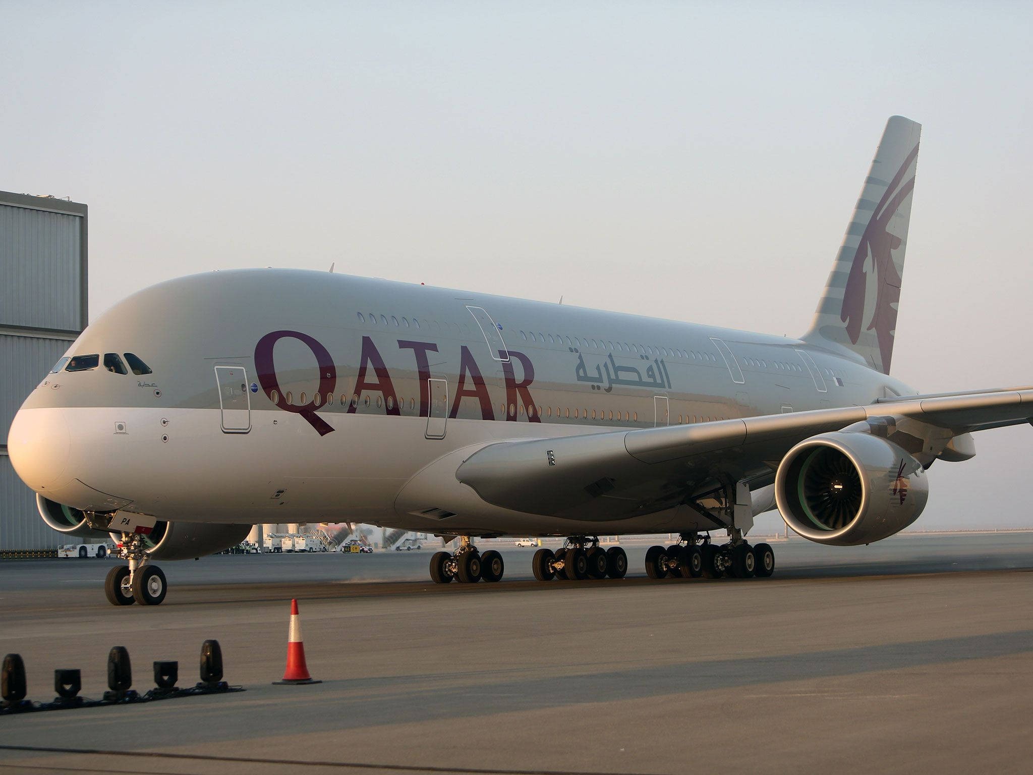 Qatar 桌布 壁紙 — 一架卡達航空的空中巴士A380停泊在機場停機坪上，沐浴在柔和的金色日出光中。