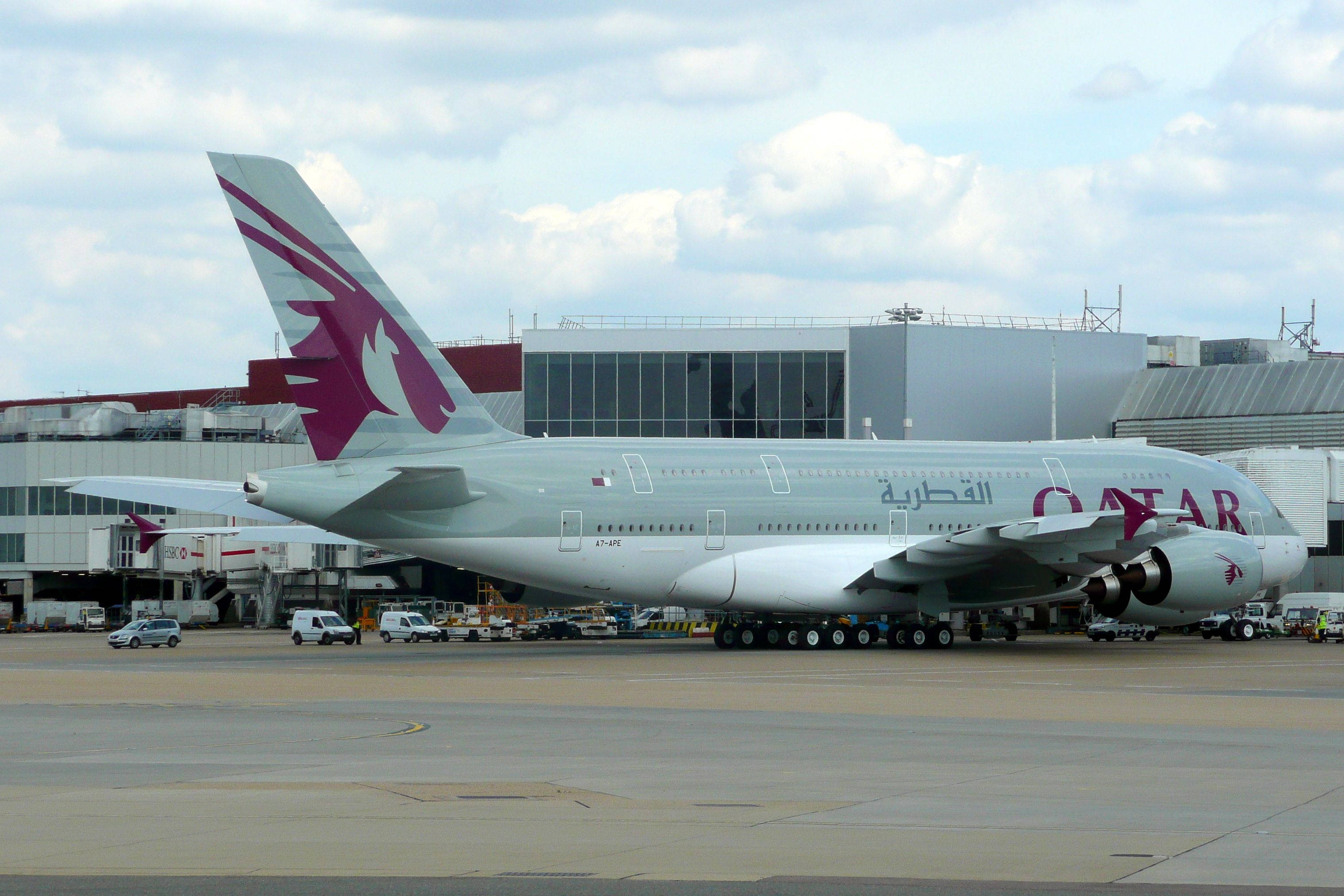 Qatar 桌布 壁紙 — 一架卡達航空空中巴士A380停泊在機場閘口，天空多雲，附近有地勤車輛。