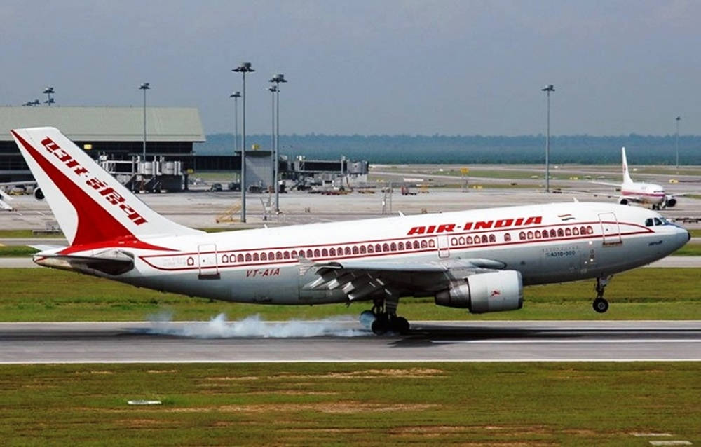 印度 桌布 壁紙 — 一架印度航空的空中巴士A300在輪子放下時降落在一條被機場基礎設施和遠處綠色山丘環繞的跑道上。