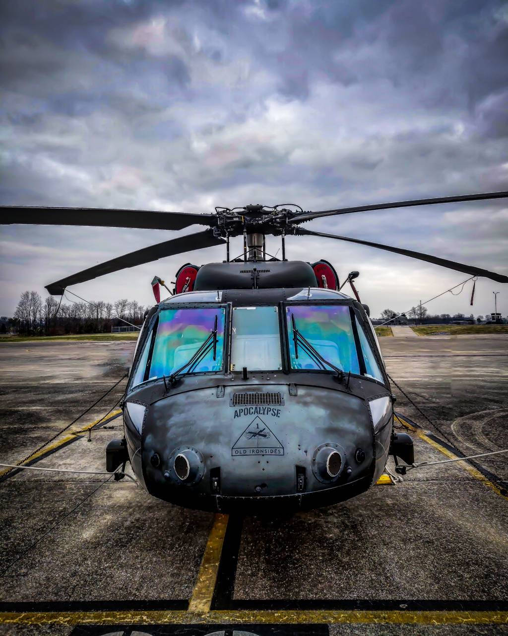 Helicopter 桌布 壁紙 — 一架名為「Apocalypse」的風化軍用直升機停在停機坪上，背景是戲劇性的多雲天空，駕駛艙窗戶閃爍著彩虹色。