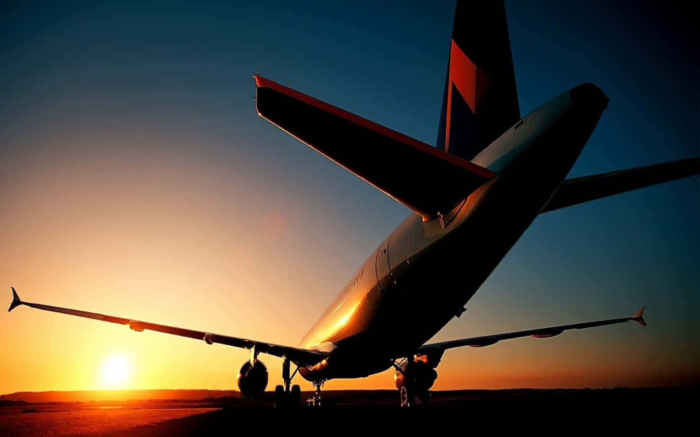 Aviation 桌布 壁紙 — 一架商用飛機在充滿活力的日落天空下呈現剪影，金色光線反射在機身上。