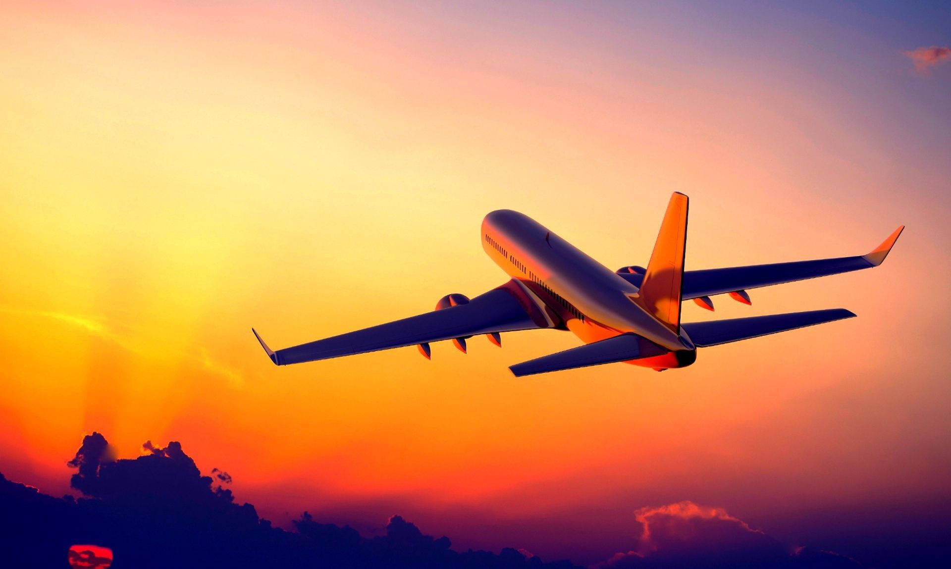 4K 飛機壁紙 桌布 壁紙 — 一架商用飛機在充滿活力的日落天空中翱翔，天空呈現橙色和紫色色調，下方有烏雲。