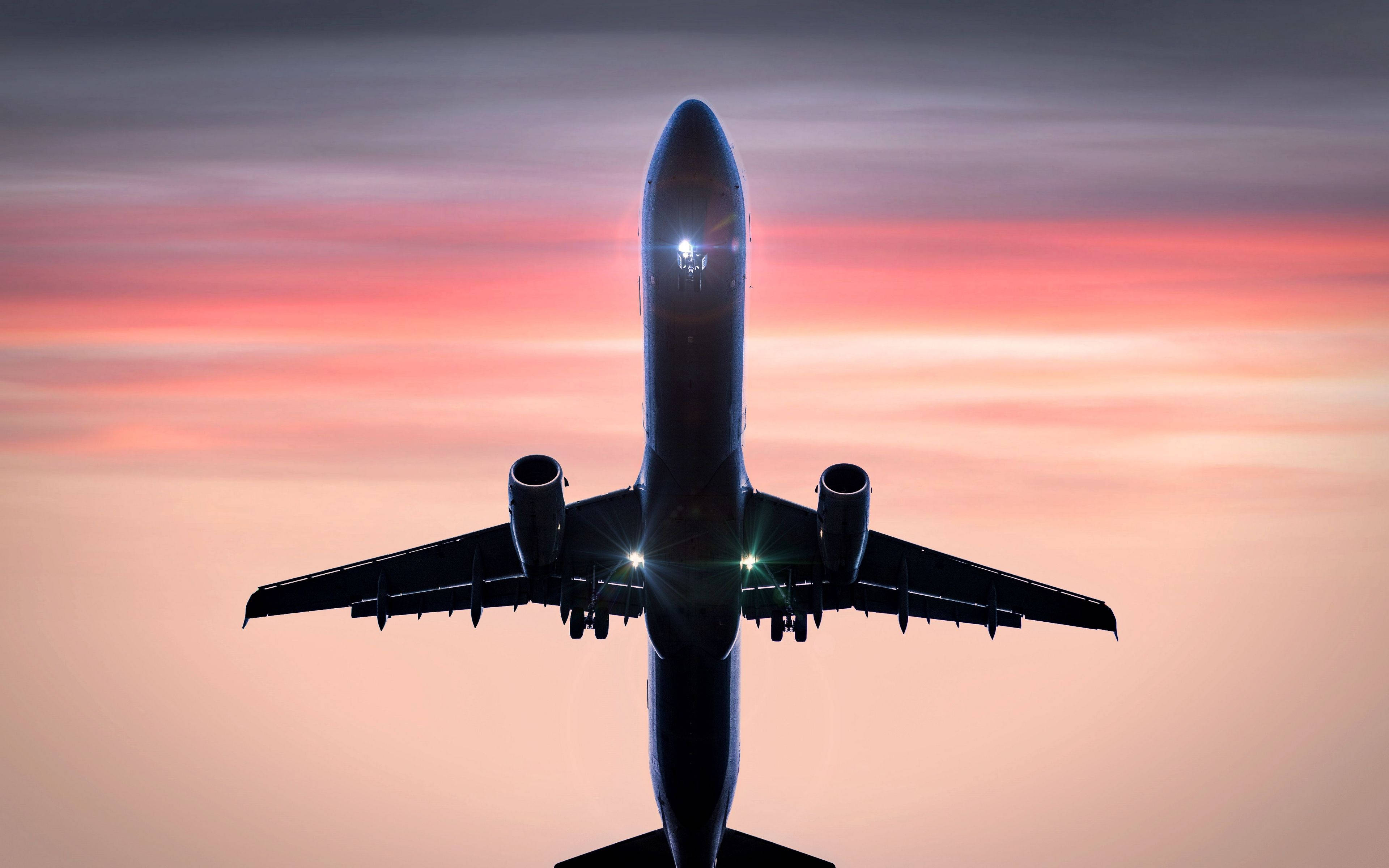 4K 飛機壁紙 桌布 壁紙 — 一架商用飛機在充滿活力的粉紅色和橙色日落天空下形成剪影，駕駛艙燈光閃爍。