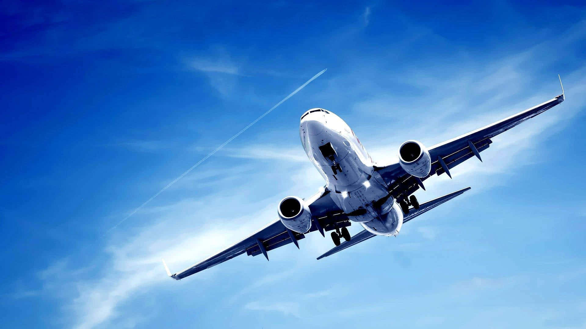 Aviation 桌布 壁紙 — 一架商用飛機在充滿活力的藍天中翱翔，伴隨著縷縷白雲和可見的凝結尾跡。