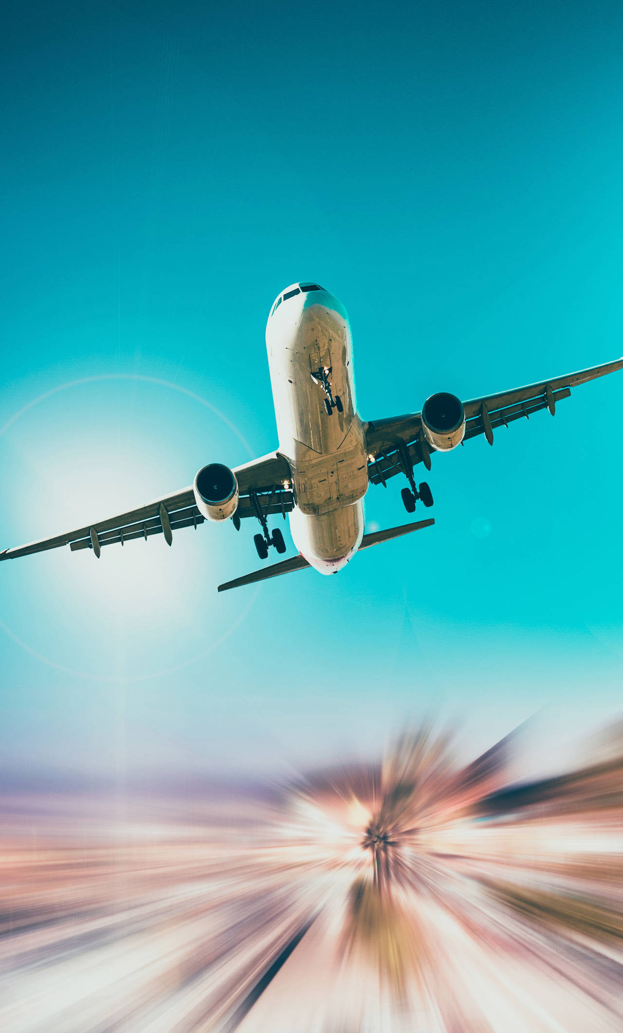 飛機 桌布 壁紙 — 一架商用飛機在充滿活力的藍綠色天空背景下翱翔，帶有太陽爆發效果和下方模糊的地面運動。