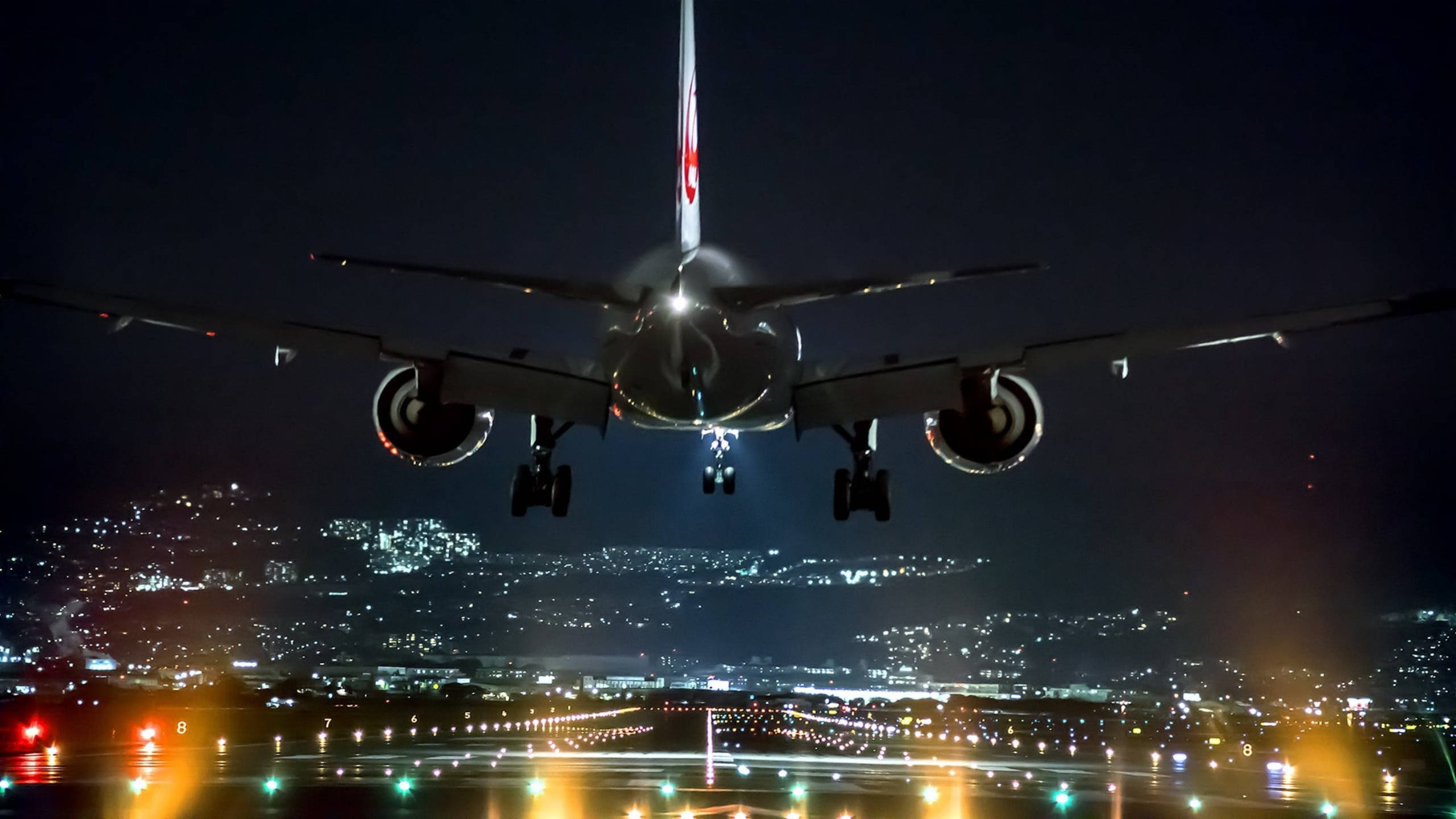 Runway 桌布 壁紙 — 一架商用飛機在夜間下降，降落燈亮著，下方是發光的城市景觀。