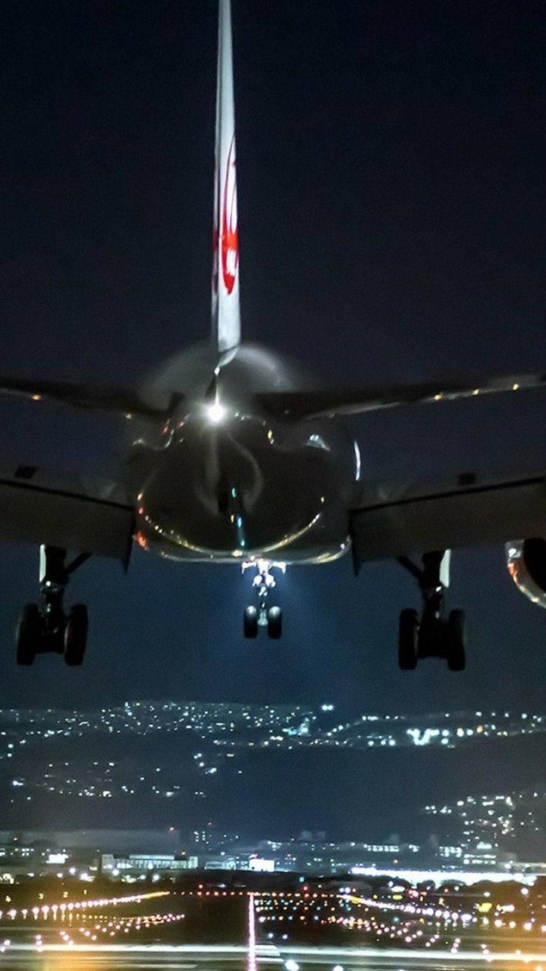 飛機 桌布 壁紙 — 一架商用飛機在夜間下降，降落燈光在下方閃爍的城市景觀中發光。