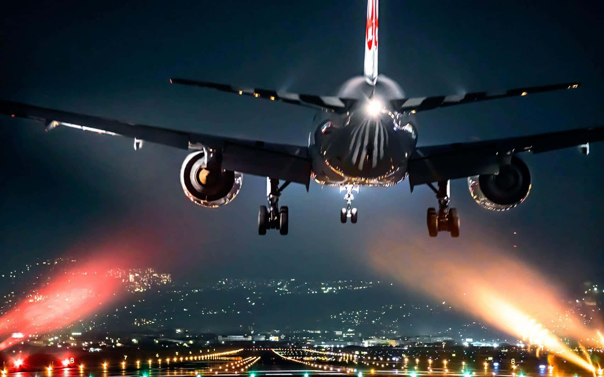飛機 桌布 壁紙 — 一架商用飛機在夜間下降，降落燈照亮跑道和下方的城市景觀。