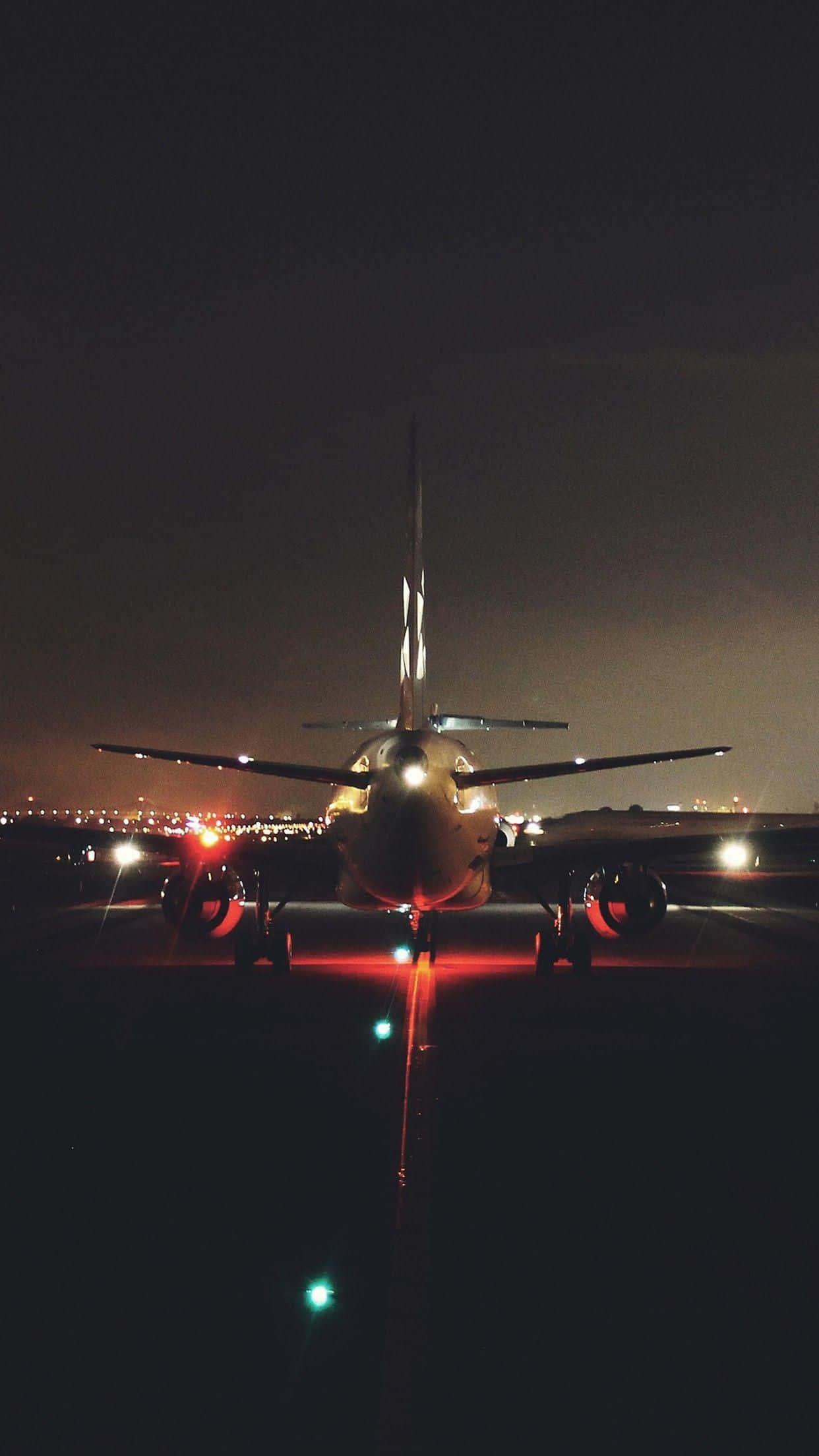 Plane 桌布 壁紙 — 一架商用飛機在夜間停在跑道上，背景有發光的紅燈和遠處的城市燈光。