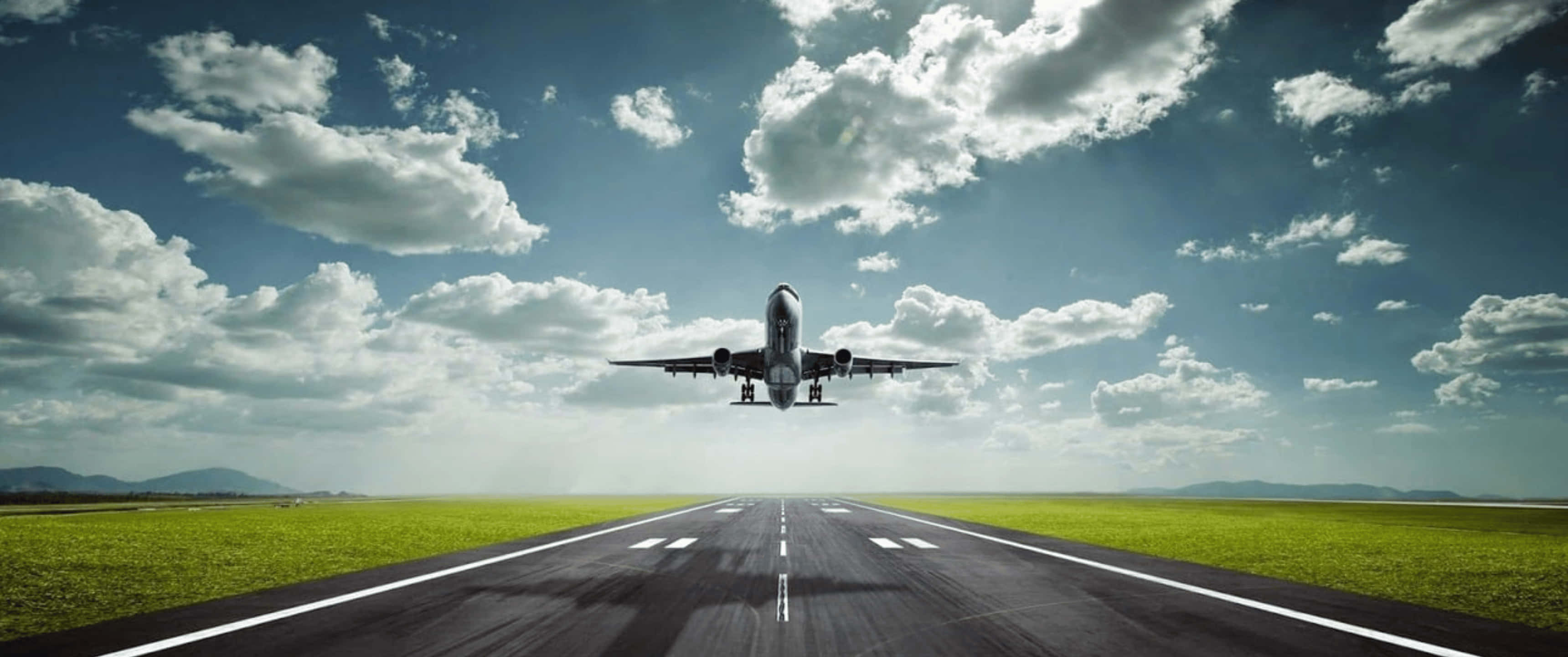 Plane 桌布 壁紙 — 一架商用飛機在戲劇性的多雲天空下，向著兩旁是翠綠田野的跑道下降。