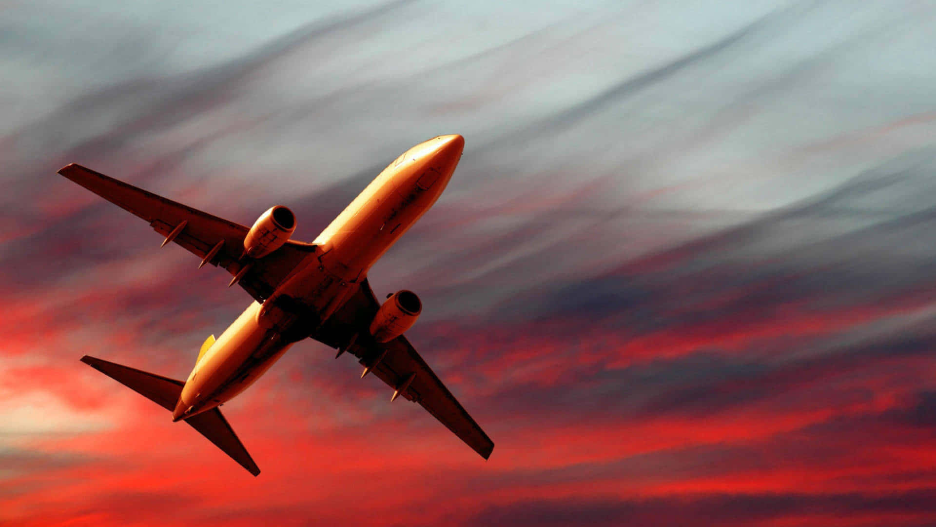 Aviation 桌布 壁紙 — 一架商用飛機在日落時分，於被火紅與深藍雲彩繪成的戲劇性天空中翱翔。