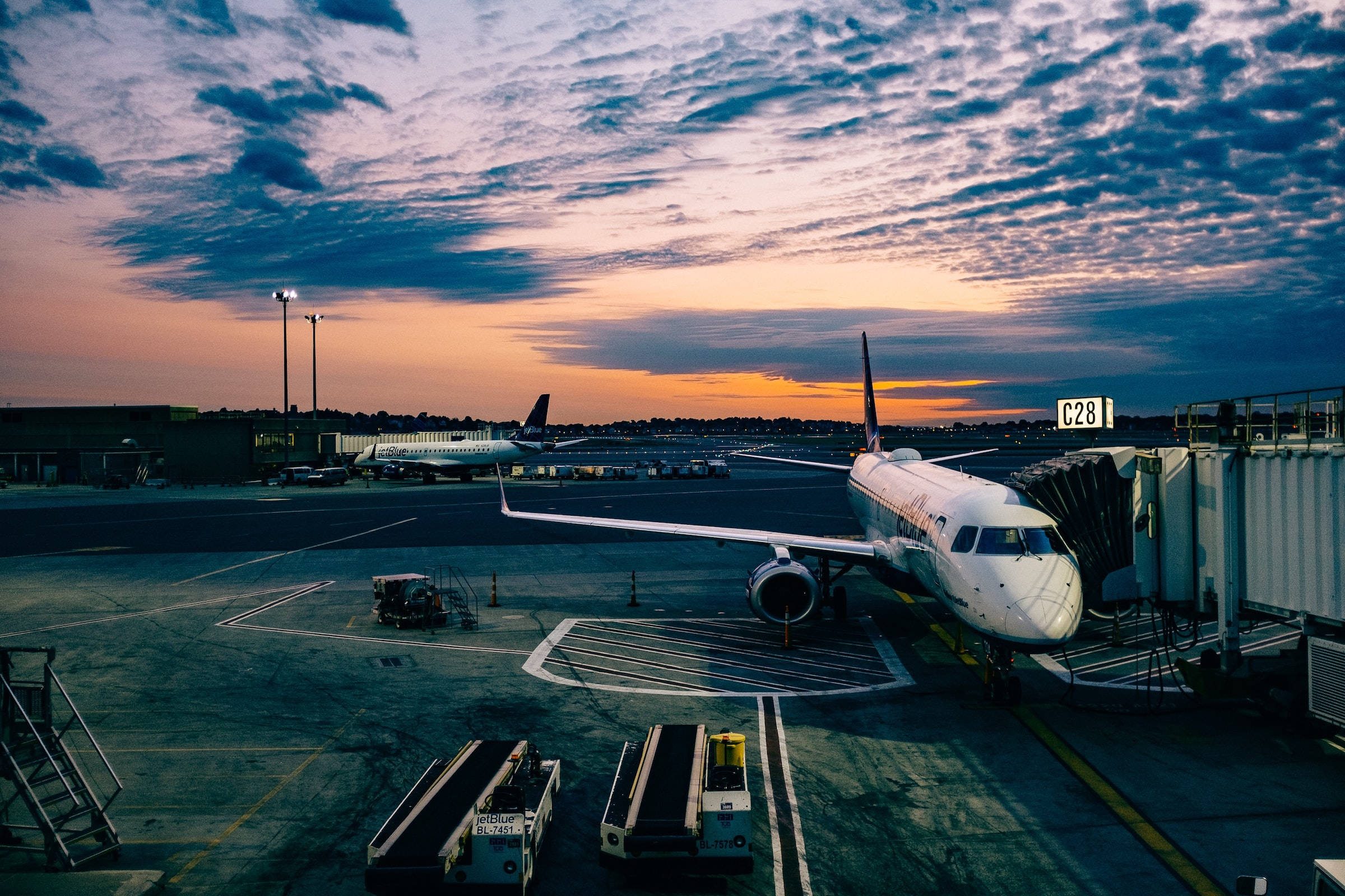 雲朵 桌布 壁紙 — 一架商用飛機在日落時分停在機場停機坪上，上空有鮮豔的橙色和紫色雲彩。