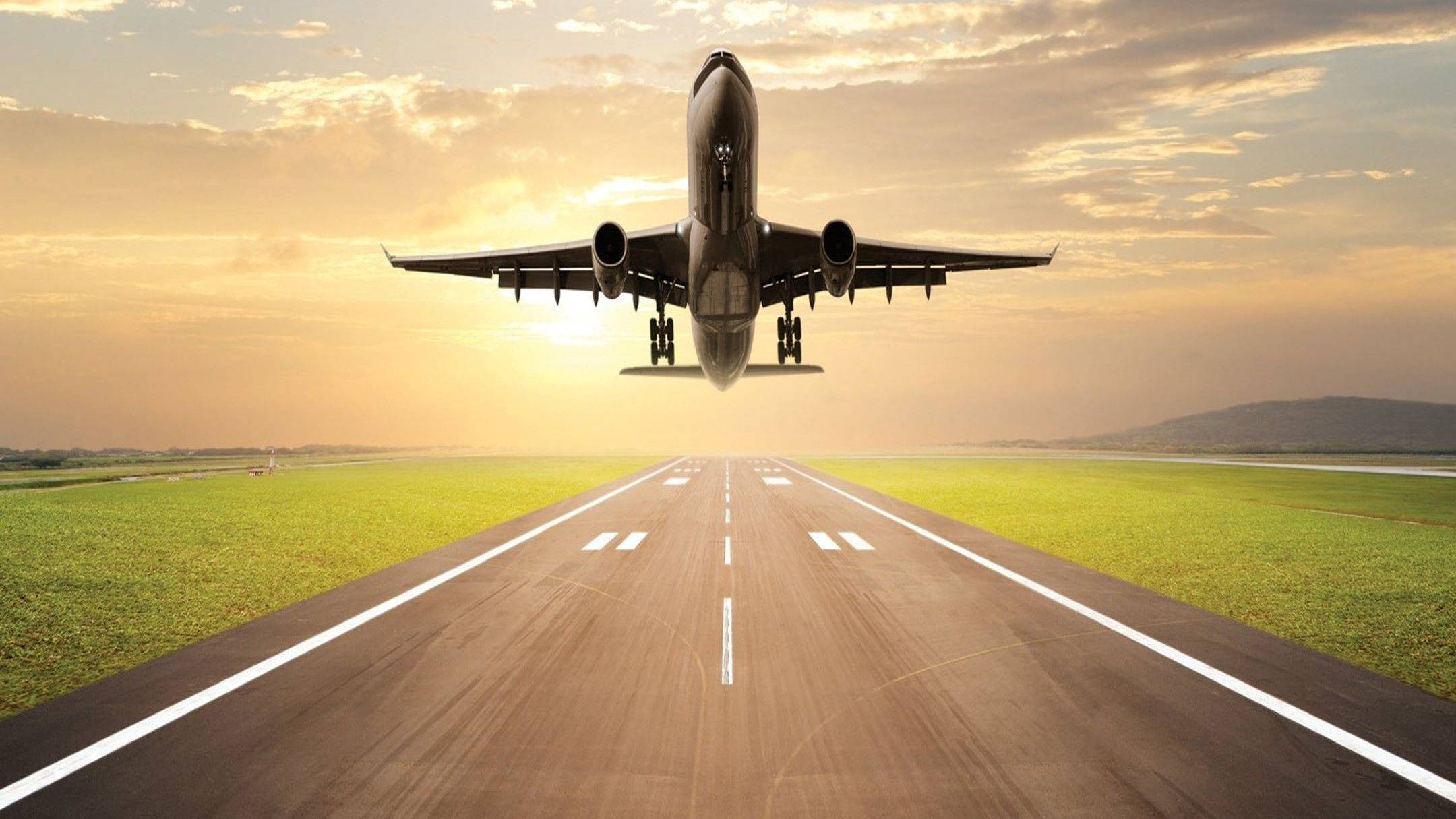 Runway 桌布 壁紙 — 一架商用飛機在日落時從跑道上升，將金色光芒灑在停機坪和綠色田野上。
