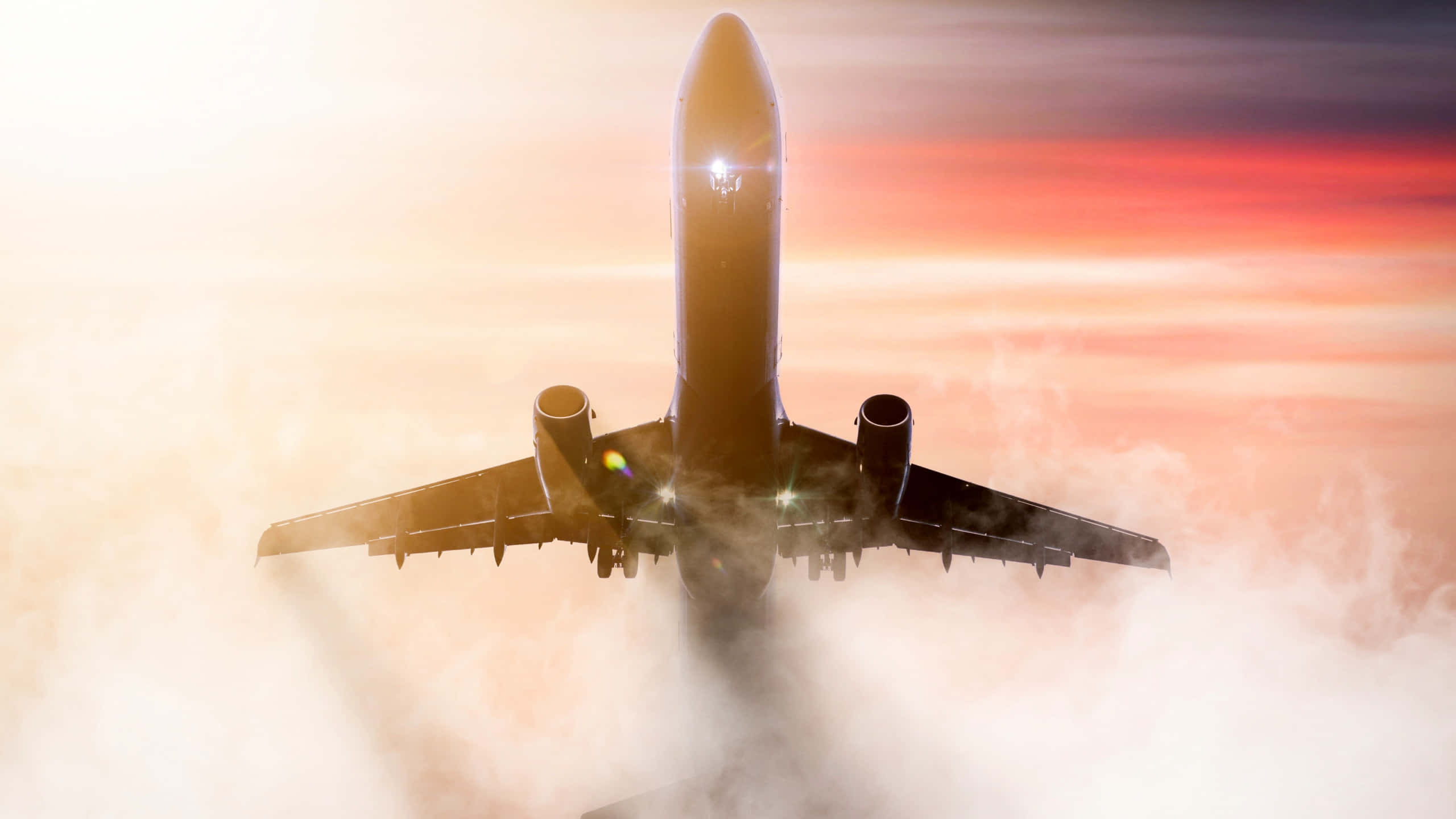 1440p Plane 桌布 壁紙 — 一架商用飛機在日落時翱翔於雲層之上，引擎發光，天空呈現火熱的橙色。