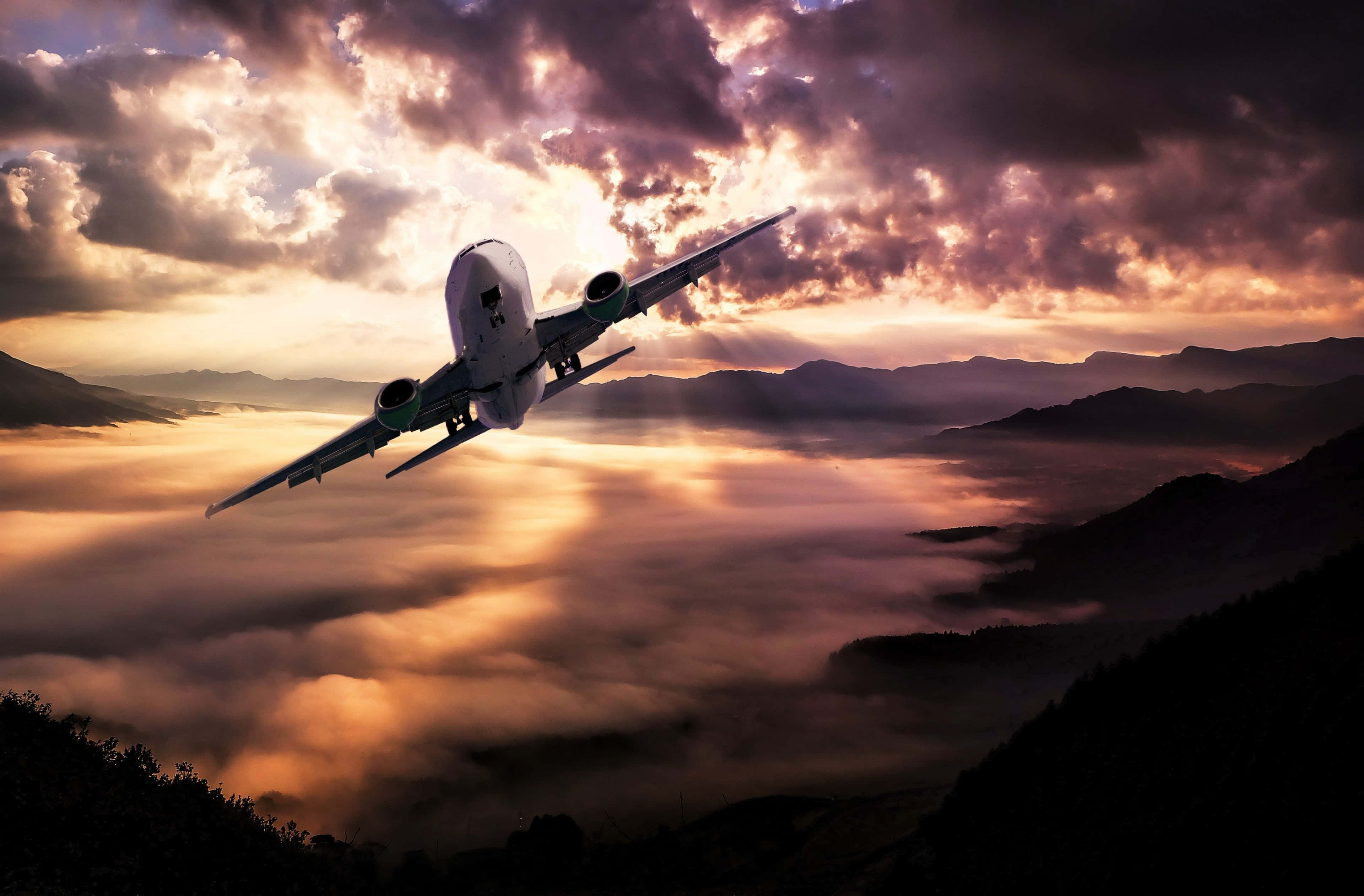 Plane 桌布 壁紙 — 一架商用飛機在日落時翱翔於雲海之上，下方是山巒的剪影。