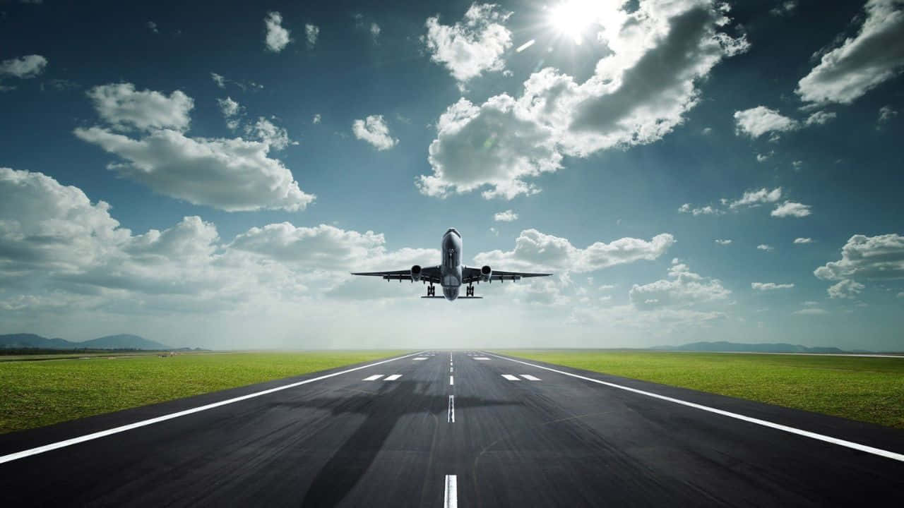 720p Plane 桌布 壁紙 — 一架商用飛機在明亮的陽光和零星雲朵下從跑道上升。