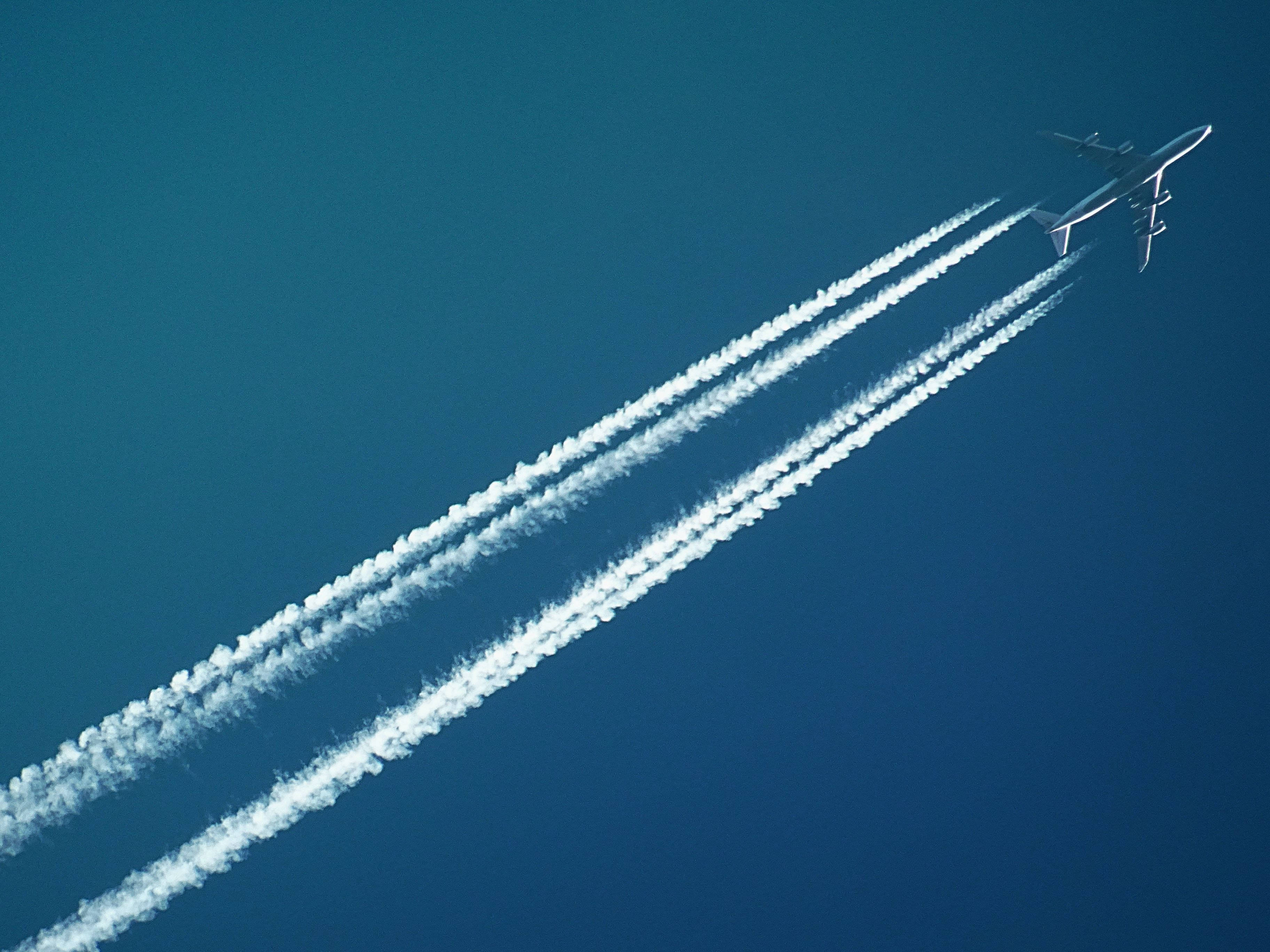Plane 桌布 壁紙 — 一架商用飛機在晴朗的藍天中翱翔，留下三條清晰的白色彩虹雲。