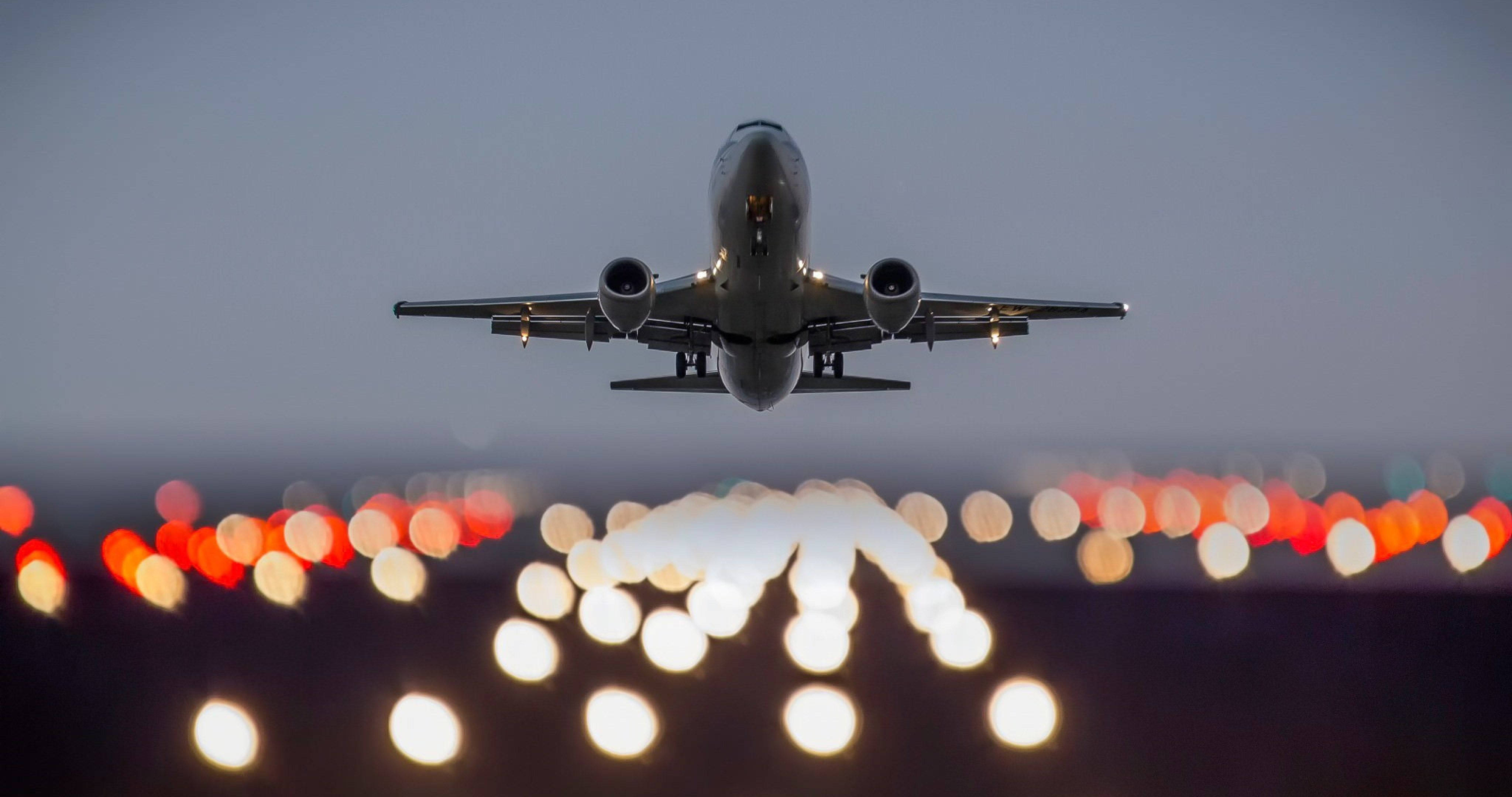 4K 飛機壁紙 桌布 壁紙 — 一架商用飛機在暮色中向著被模糊散景燈光照亮的跑道下降。