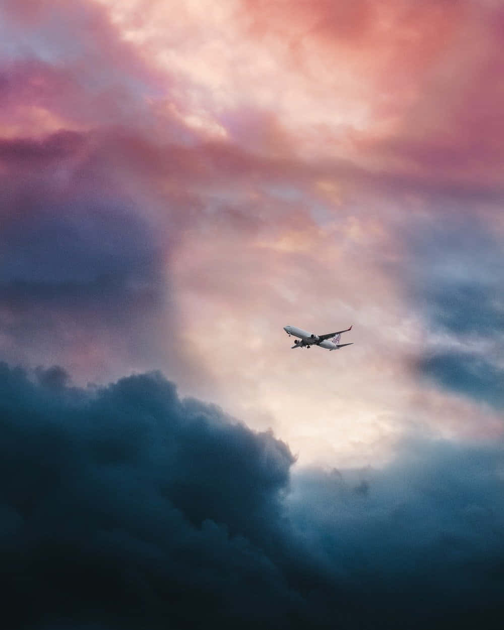 Plane 桌布 壁紙 — 一架商用飛機在暮色中翱翔於由粉紅、紫色和深藍色雲彩繪成的戲劇性天空。