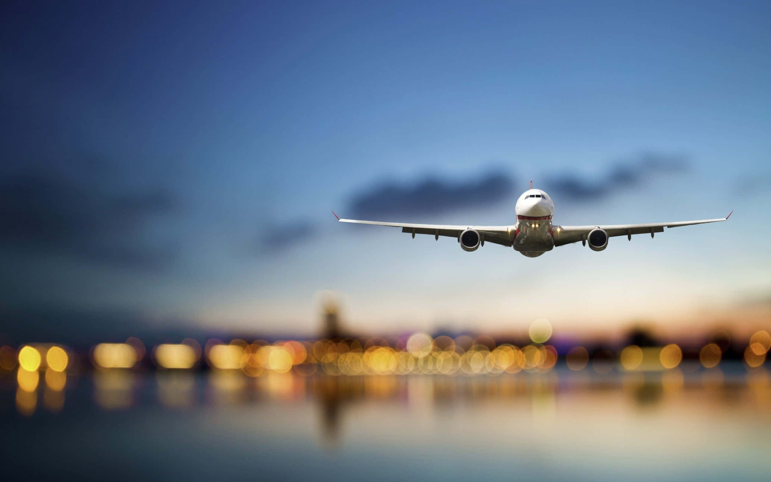4K 飛機壁紙 桌布 壁紙 — 一架商用飛機在暮色天空下向著倒映在水中的城市天際線下降。