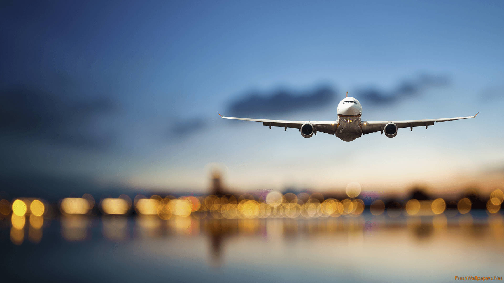Plane 桌布 壁紙 — 一架商用飛機在暮色天空中飛過，下方模糊的城市燈光倒映在水面上。