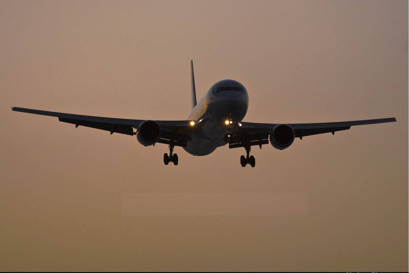 Plane 桌布 壁紙 — 一架商用飛機在柔和的橙色暮色天空中下降，降落燈閃爍著光芒。