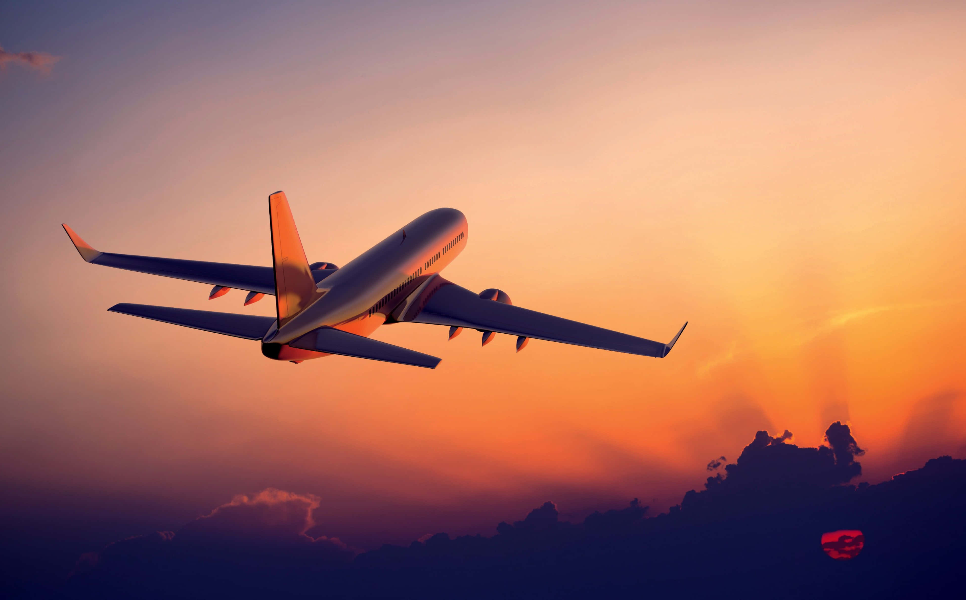 Plane 桌布 壁紙 — 一架商用飛機在橙紫色調的鮮豔日落天空中翱翔，飛越輪廓分明的雲層。