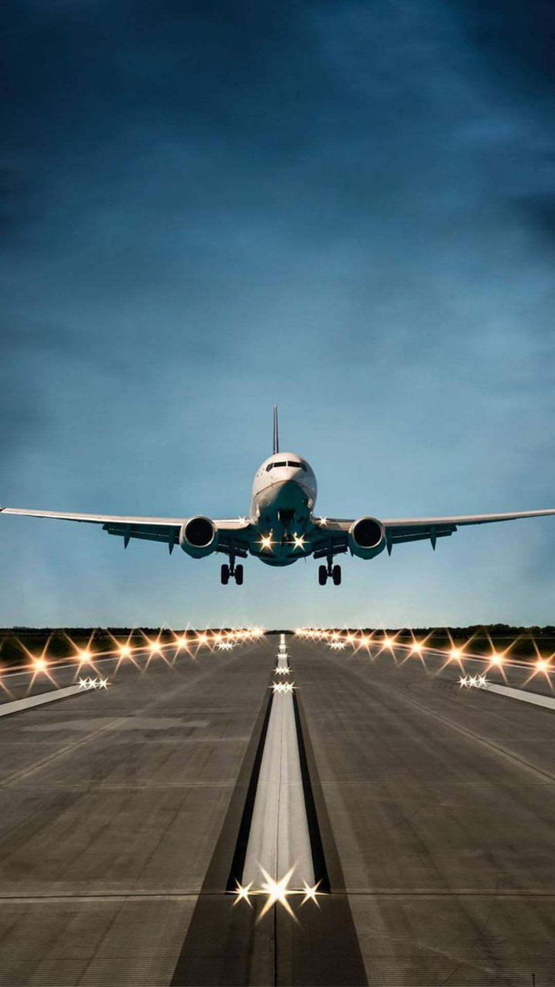 Runway 桌布 壁紙 — 一架商用飛機在深藍色暮色天空下，低飛過被發光燈光照亮的跑道。