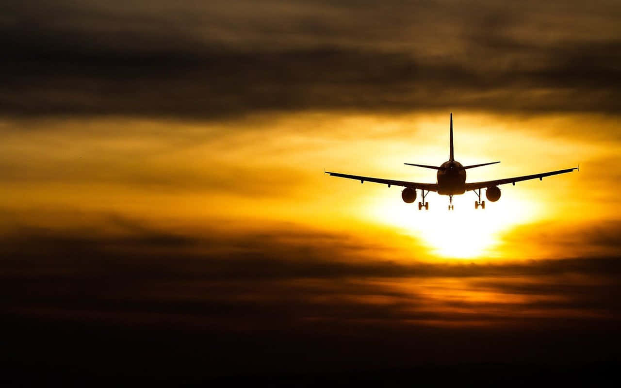 飛機 桌布 壁紙 — 一架商用飛機在熾熱的日落天空和發光的雲層襯托下呈現剪影。