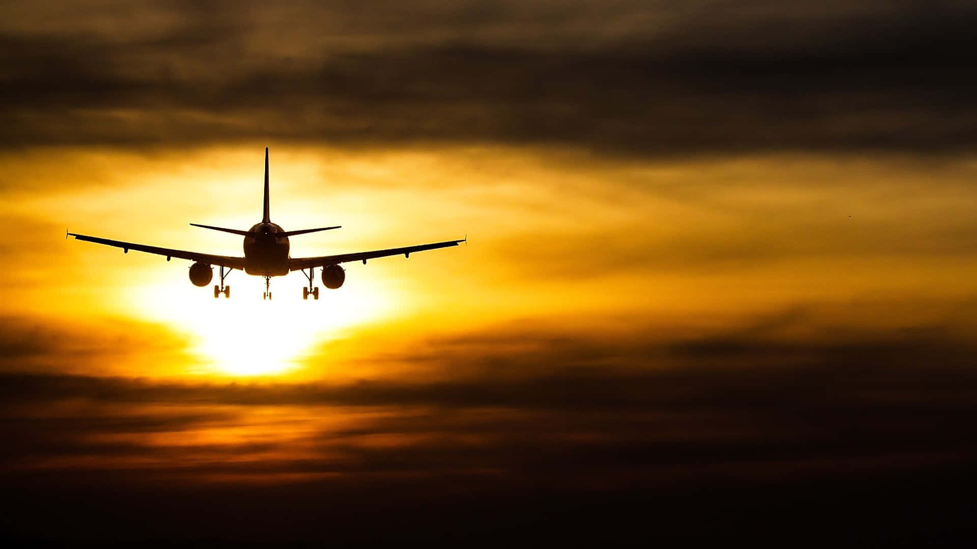 飛機 桌布 壁紙 — 一架商用飛機在熾熱的日落天空和發光的雲層襯托下形成剪影。