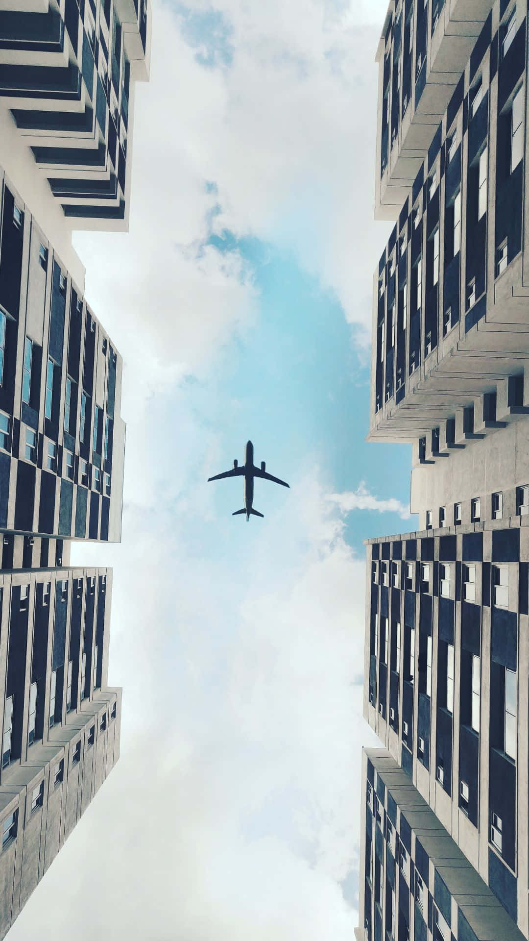 飛機在藍天白雲下飛越城市高樓之間。 — 飛機 壁紙