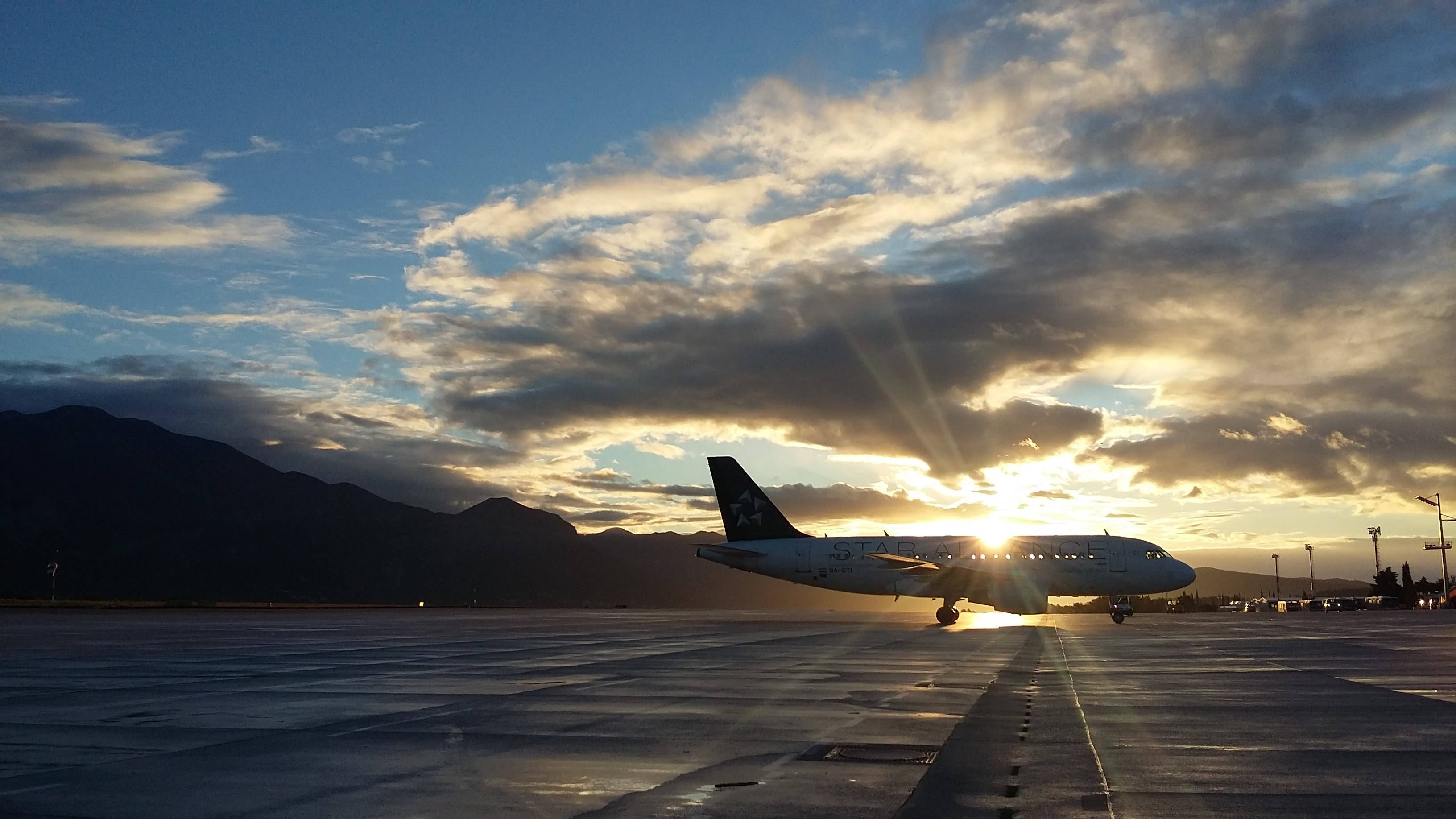 Plane 桌布 壁紙 — 一架商用飛機在金色日落、戲劇性雲層和遠山背景下形成剪影。